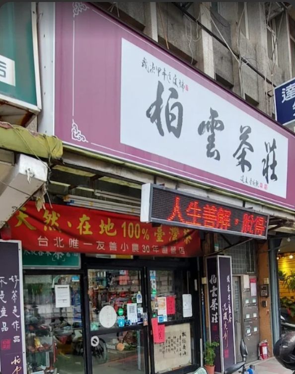 柏雲茶莊店門口，粉紫色招牌上有「柏雲茶莊」毛筆大字，玻璃門上方掛著「天然、在地 100% 臺灣茶」紅色布條